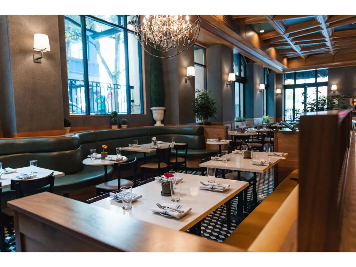 An elegant dining area glows with a central chandelier, abundant greenery, and decorative wall panels. Guests celebrate, dine, and toast in a setting that feels both upscale and relaxed, suggesting the social and culinary experiences the hotel provides.