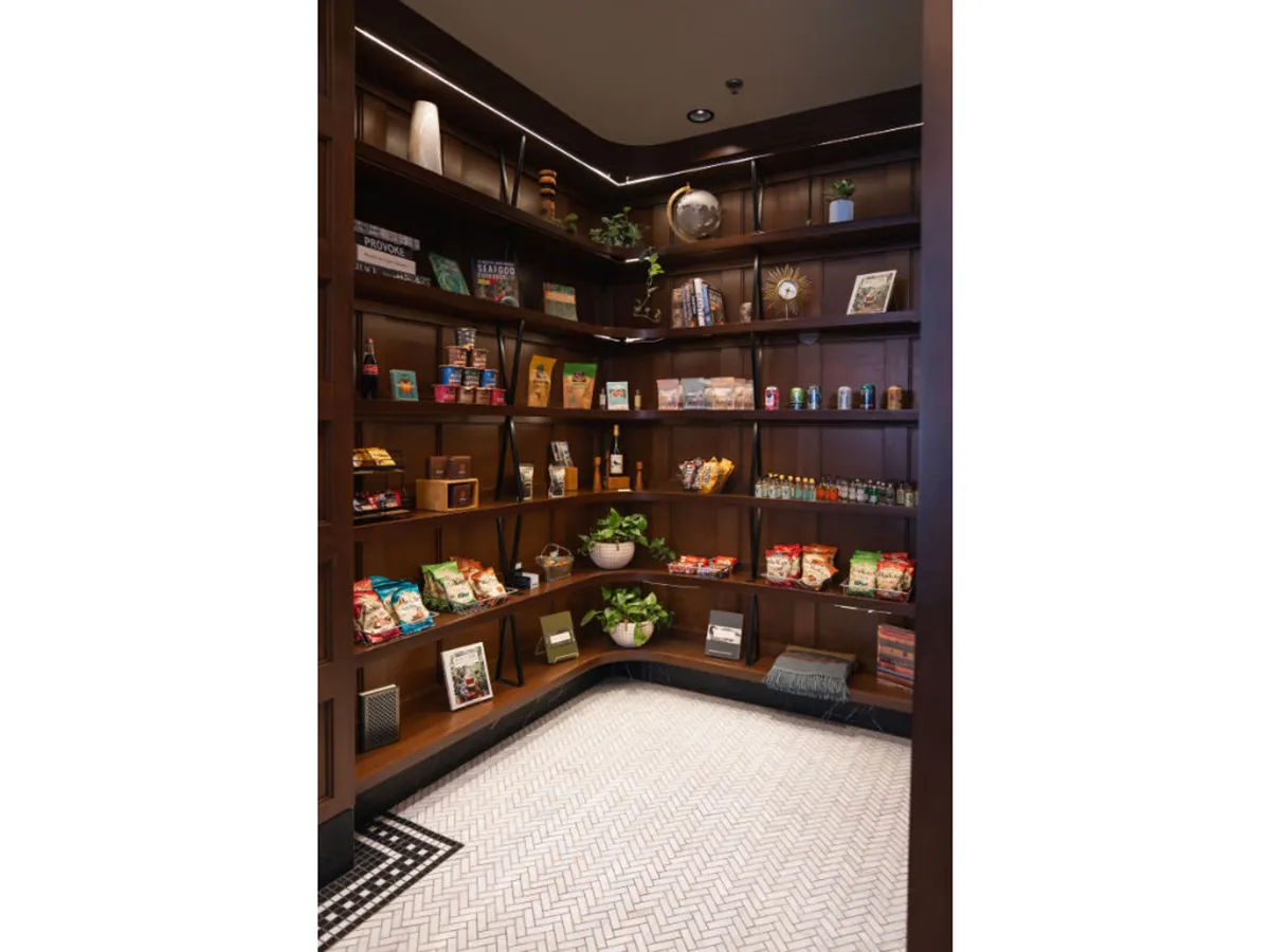 This cozy corner displays shelves filled with snacks, decorative items, a potted plant, and an interesting floor pattern. The setting is inviting, with a warm, home-like vibe that suggests comfort and thoughtful amenities for guests.