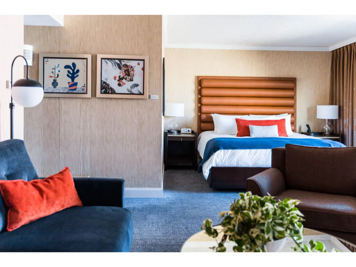 This image showcases a comfortable bedroom featuring a bed with decorative pillows, eye-catching artwork on the wall, and stylish furniture. The setting is modern and serene, evoking a sense of relaxation and home-like luxury ideal for resting after city adventures.