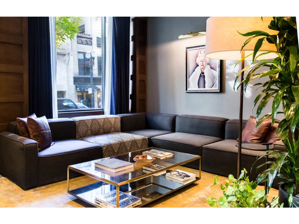 A chic and comfortable sitting area with a stylish sofa, coffee table, elegant lamp, and artwork on the wall. Nearby plants bring a touch of nature indoors, while the arrangement exudes a blend of sophistication and warmth.