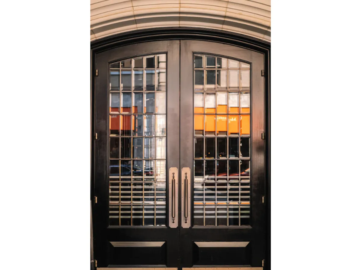An exterior shot featuring ornate double doors with intricate glass design and stylish door handles, suggesting an inviting and sophisticated entry to the property. The view captures the anticipation of entering a vibrant, urban lifestyle setting.